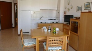 Eine kompakte Küche mit weißen Schränken, einem Esstisch mit Stühlen und einem kleinen Fernseher auf einem Schrank.