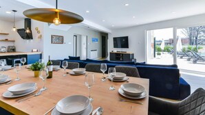 Una sala de estar moderna con comedor, televisor y un amplio ventanal con vista a una piscina.
