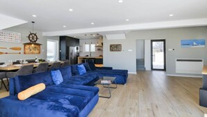 Una sala de estar moderna con un amplio sofá azul, un comedor con mesa de madera y una cocina al fondo.