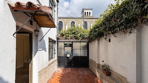 Une ruelle étroite avec un sol carrelé, une porte noire et, au fond, un bâtiment doté d’un toit en tuiles et de fenêtres en arc de cercle.