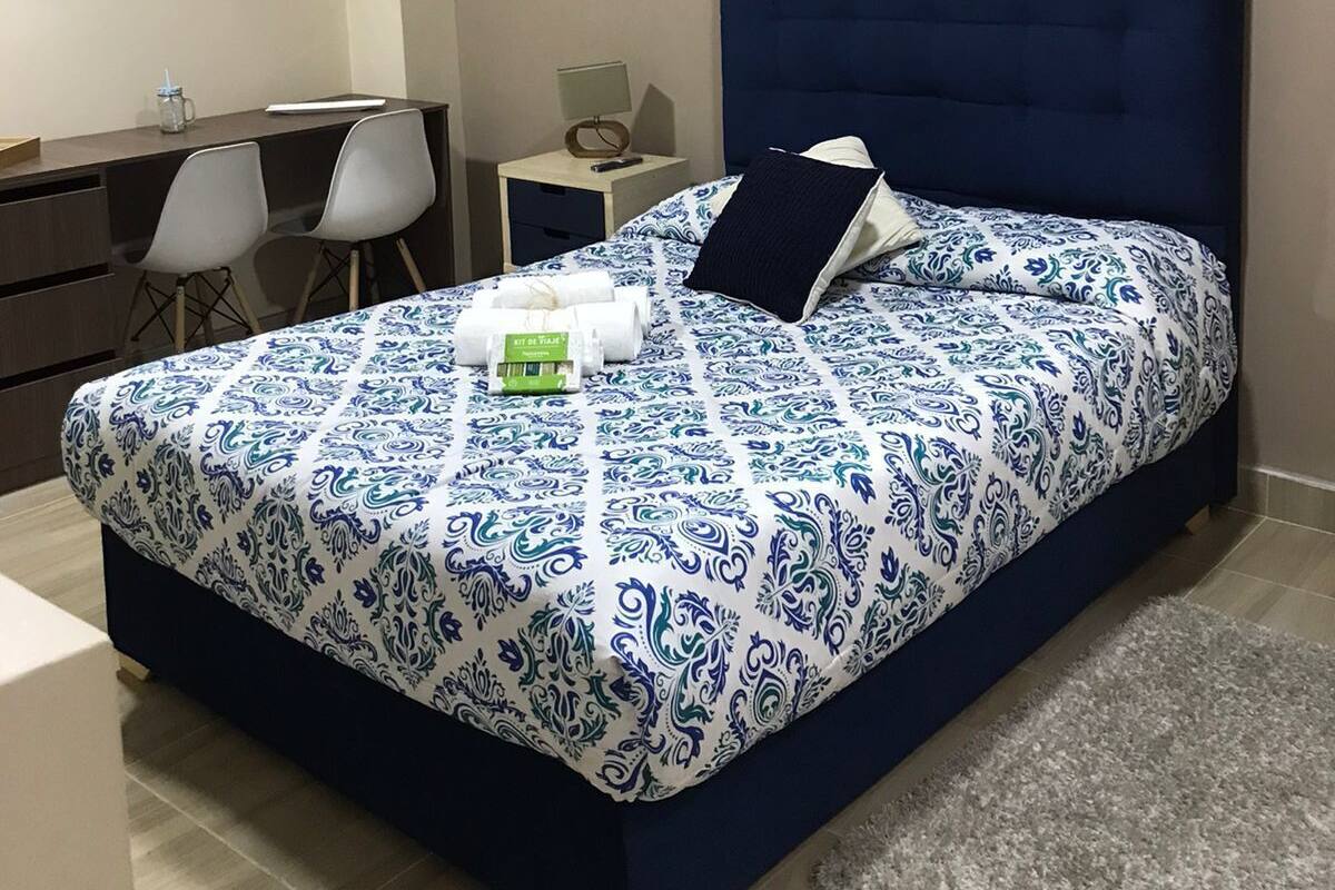 Un dormitorio con cama, mesita de noche, lámpara y un escritorio con sillas.