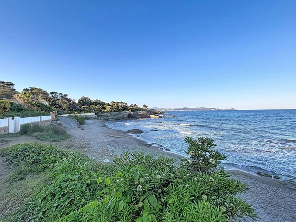 A coastal road with a rocky beach, a white fence, and greenery.
