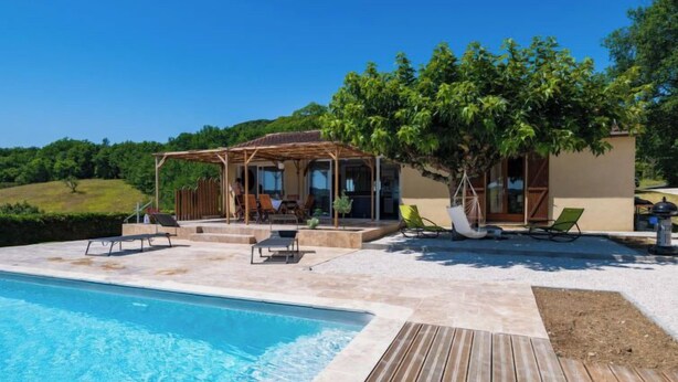 Un área junto a la piscina con una terraza de madera, sillas de descanso y un espacio de estar cubierto.