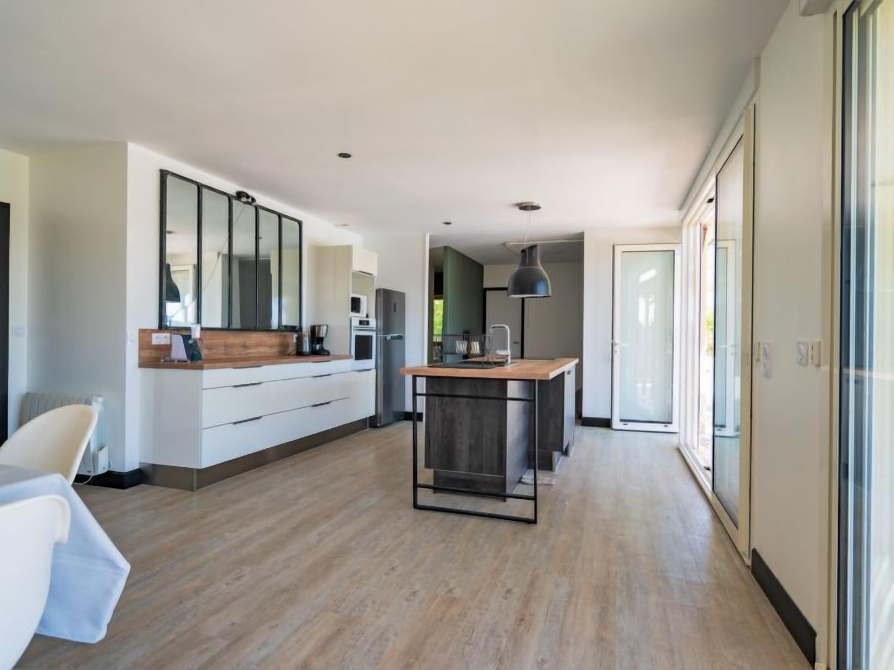 Et moderne køkken med en central ø, et stort spejl og en skydedør, der fører ud til en balkon.