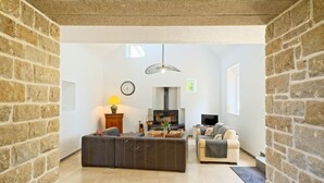 Amplia sala de estar con chimenea, un sofá, un televisor y una pared de piedra.