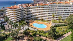 Um hotel alto com várias varandas, uma piscina e vista para o mar.
