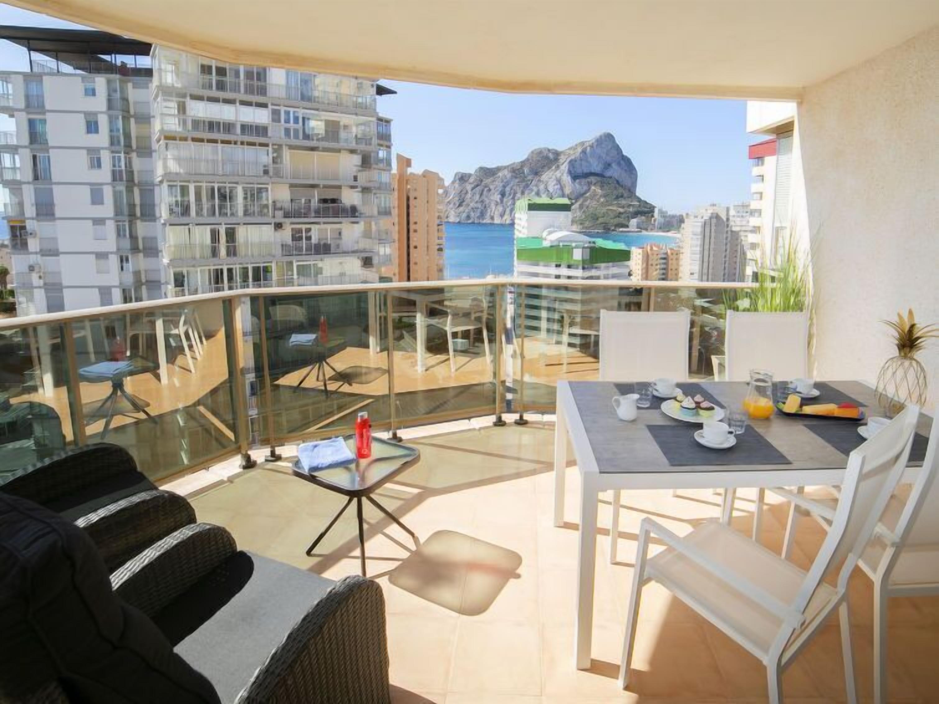 Ein Balkon mit Esstisch, gedeckt für das Frühstück, mit Blick auf eine felsige Küstenlinie und weitere Gebäude.