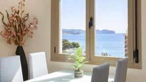 Ein Zimmer mit großem Fenster und Blick auf die Küste, eine Vase mit Blumen und eine kleine Pflanze am Fensterbrett.
