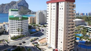 Ein Hochhaus-Hotel mit rotem Dach, Schwimmbecken und Blick auf Meer und Berge.