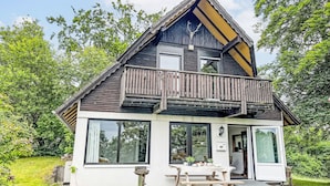 Ett modernt hus med en balkong, stora fönster och en liten uteplats.