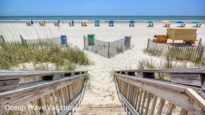 A beach with rows of sun loungers and umbrellas, a wooden fence, and a clear view of the ocean. - Amazing Beach Condo with Water Park at Dunes Village Resort (Myrtle Beach)