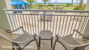 A balcony with two chairs and a table, overlooking a beach with umbrellas and palm trees. - Amazing Beach Condo with Water Park at Dunes Village Resort (Myrtle Beach)