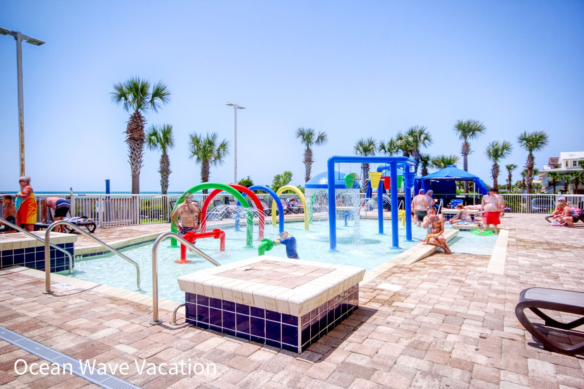 A pool area with a water play structure, lounge chairs, and palm trees.