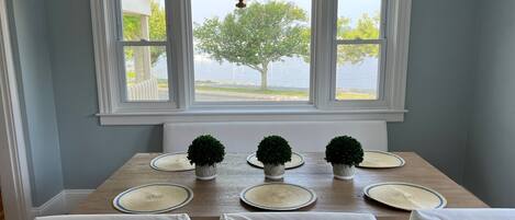 Un coin repas avec une table en bois, des chaises blanches et une vue sur un lac, visible à travers de grandes fenêtres.