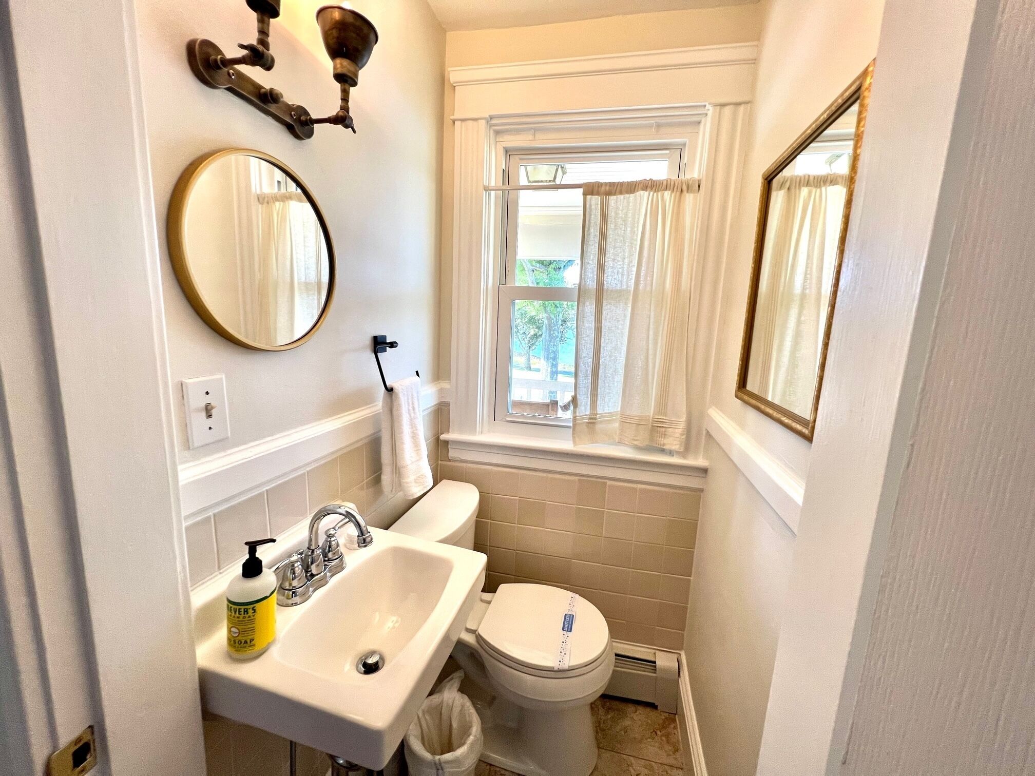 A compact bathroom with a sink, toilet, and a window with curtains.