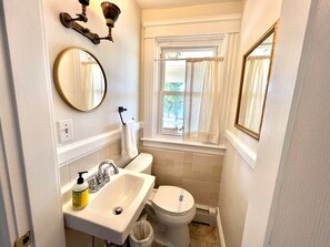 A compact bathroom with a sink, toilet, and a window with curtains. - Downtown Historical Bristol Seaside cottage w front row seats to 4th July Parade (Bristol)