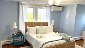 Une chambre à coucher comprenant un lit, deux tables de chevet, une commode, une fenêtre avec des rideaux, un appareil de climatisation et une porte.
