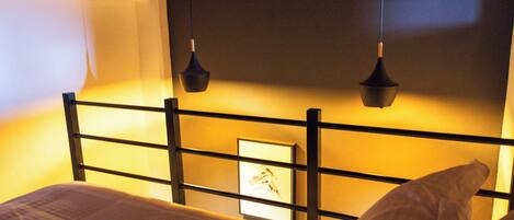 A neatly made bed with a headboard featuring a framed picture, a bedside table, and two hanging pendant lights.