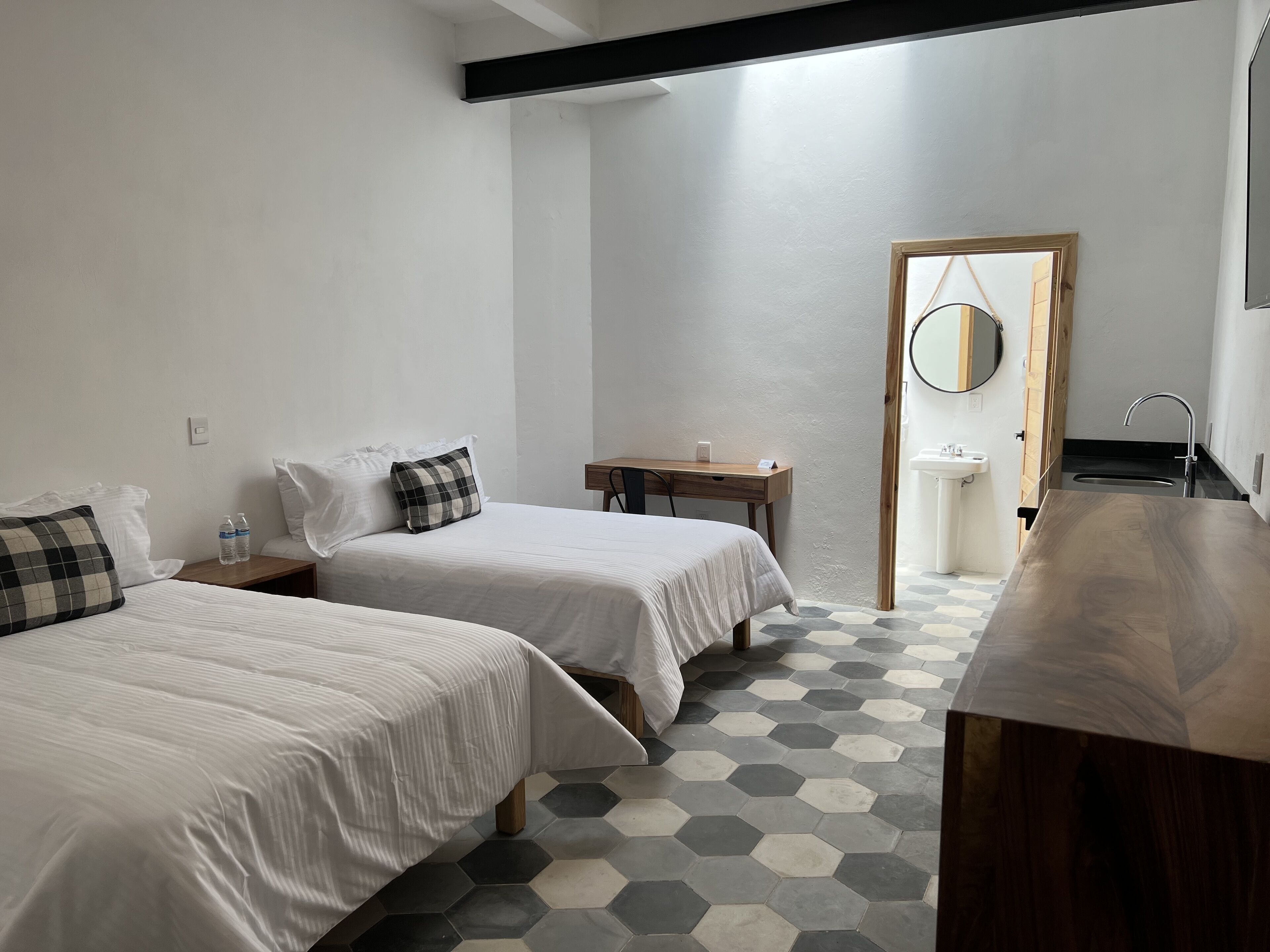 Una habitación de hotel con dos camas, un escritorio, un espejo y un baño.