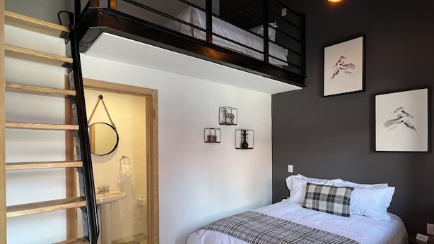 Un dormitorio con cama, una escalera de madera, un baño pequeño y una escalera que sube a un nivel superior.