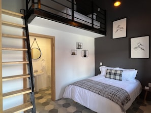 Un dormitorio con cama, una escalera de madera, un baño pequeño y una escalera que sube a un nivel superior.