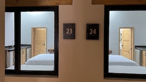 Una habitación con dos espejos, cada uno reflejando una cama y una puerta. Los números 23 y 24 están exhibidos en la pared entre los espejos.