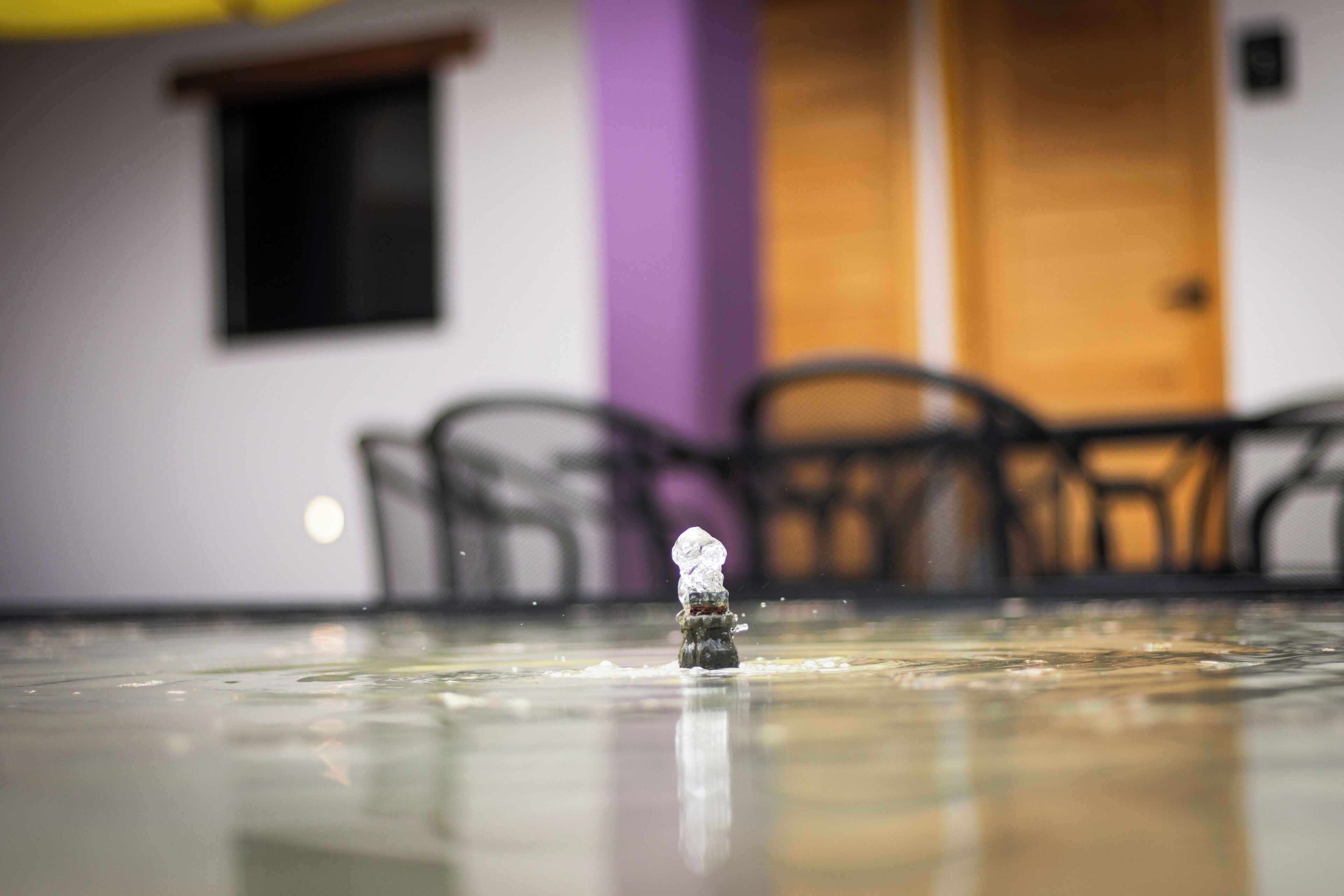 A small figurine on a reflective surface with a blurred background of chairs and a door.
