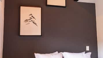 Un dormitorio con una cama, dos cuadros en la pared, un taburete de madera y una escalera.