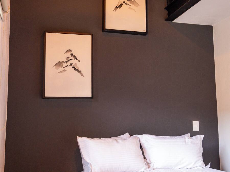 Un dormitorio con una cama, dos cuadros en la pared, un taburete de madera y una escalera.