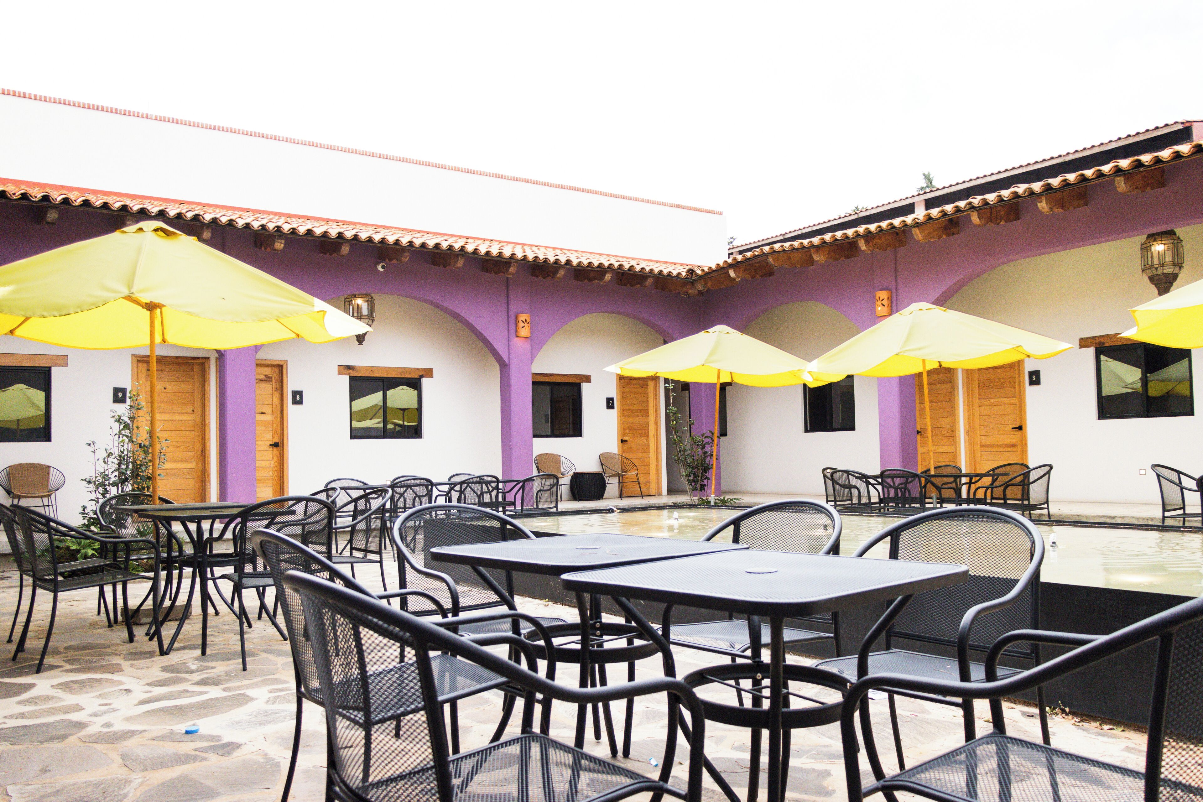 Un patio al aire libre con mesas y sillas, sombrillas amarillas y una piscina.