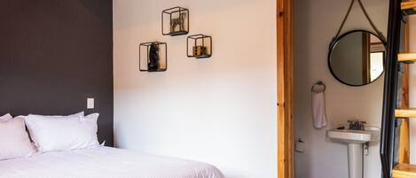 A bedroom with a bed, a wall-mounted mirror, and three cube-shaped light fixtures.