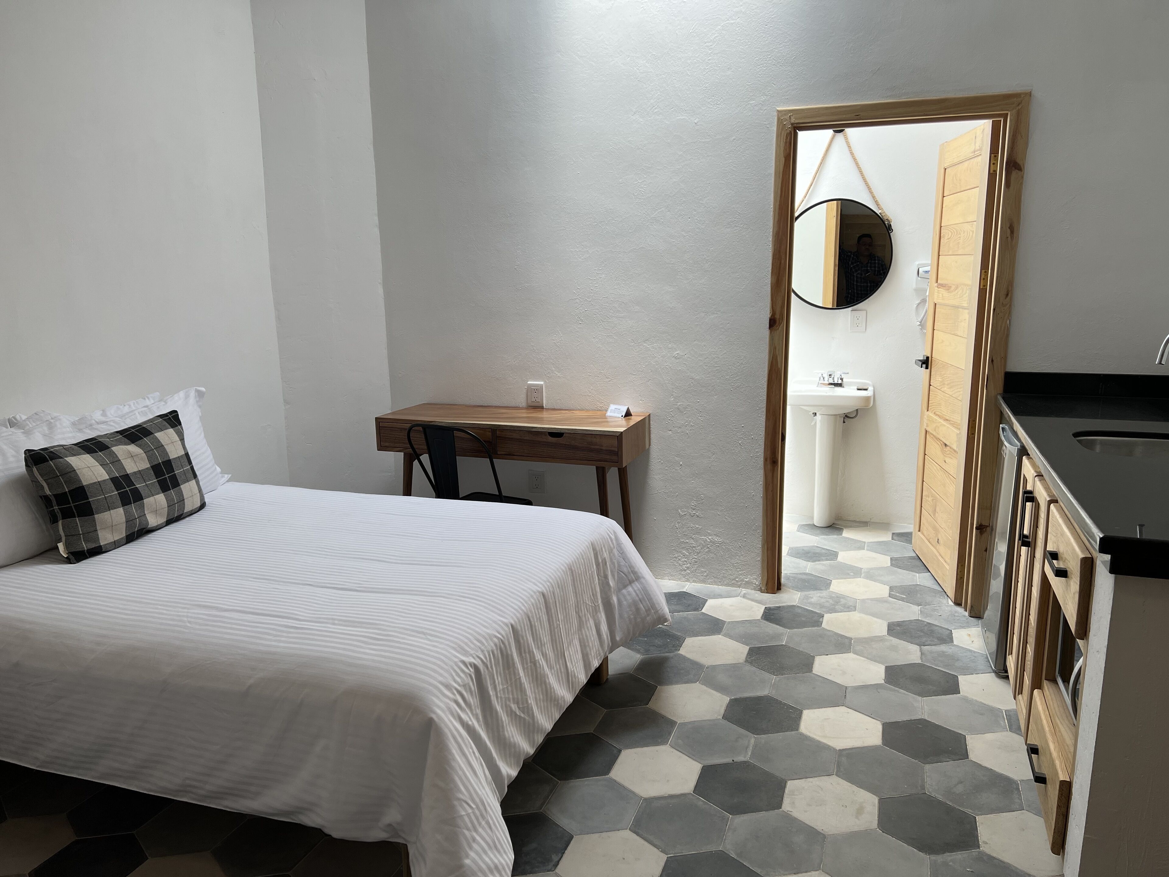 A bedroom with a bed, a desk, a mirror, and a view into the bathroom.