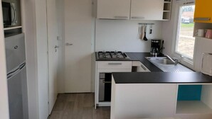 Une cuisine de taille réduite, équipée d’une cuisinière à gaz, d’un évier et de meubles blancs.