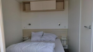 Une chambre à coucher comprenant un lit, deux tables de chevet, une tête de lit en bois et une étagère intégrée au-dessus du lit.