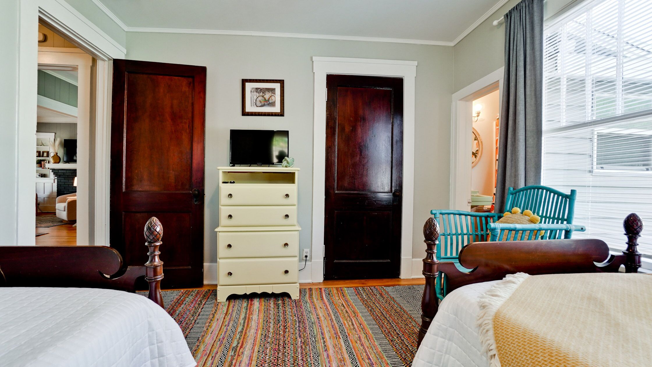 A hotel room with two beds, a dresser, a television, and a window with blinds.