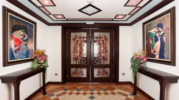 Un pasillo con suelo de baldosas, puerta de madera con paneles de vidrio y cuadros enmarcados a ambos lados.