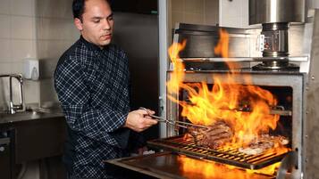 Un chef asando carne en una parrilla de alta temperatura en una cocina.