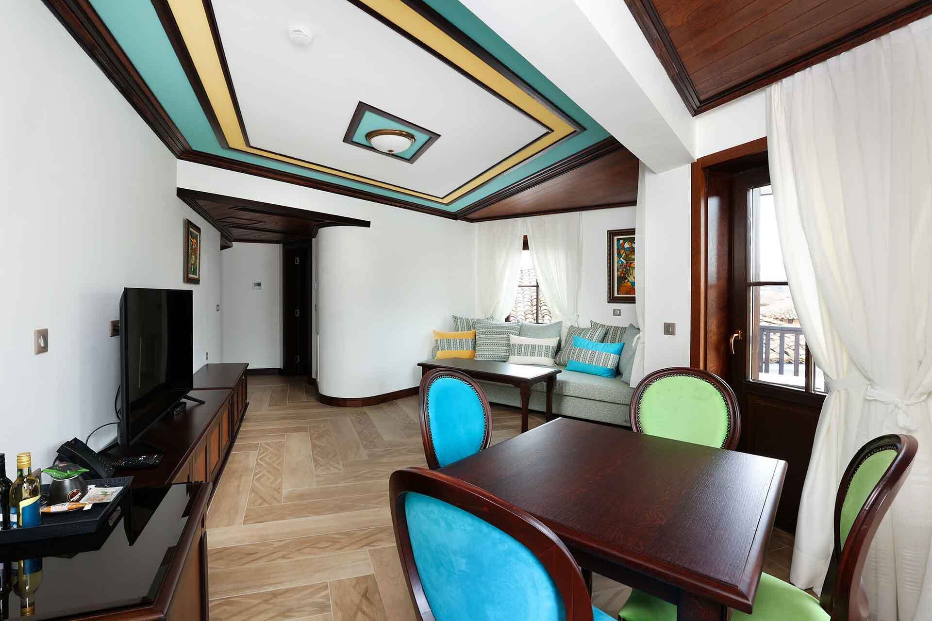 A dining area with a wooden table and chairs, a television, and a sofa with patterned cushions.