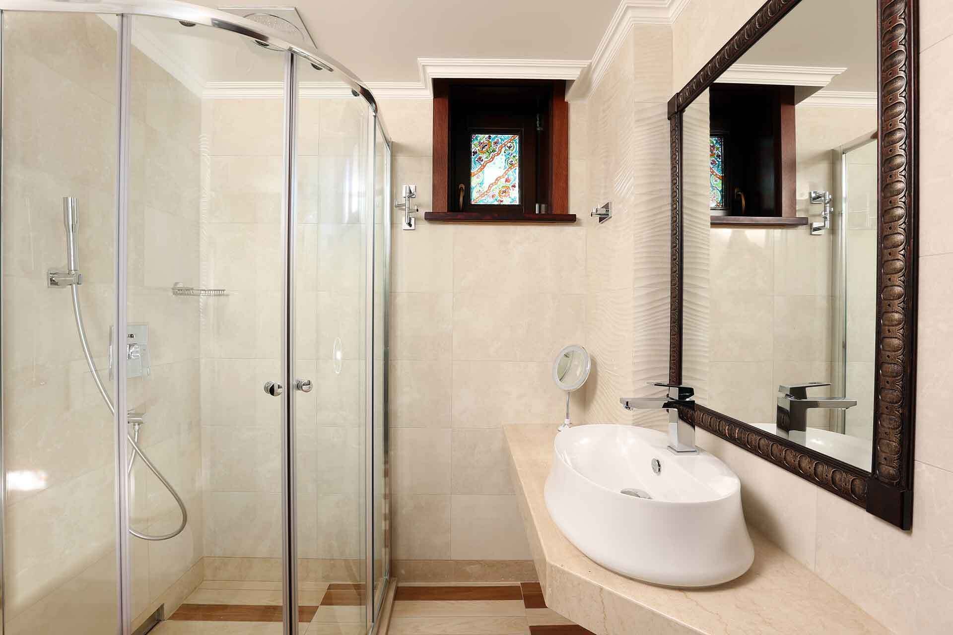 Un baño moderno con ducha envuelta en vidrio, un lavamanos blanco y un espejo grande con marco decorativo.