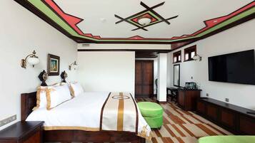A hotel room with a bed, a green ottoman, a TV, and a wooden floor.