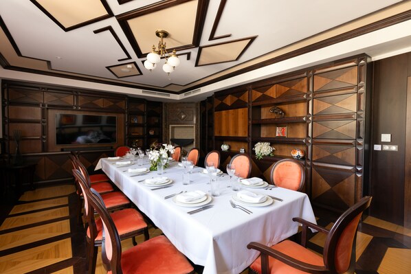 Un comedor con una mesa larga dispuesta para una comida, rodeada de sillas de madera con cojines naranjas.