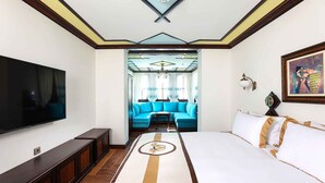 A hotel room with a large flat-screen TV, a sofa, a bed with a striped headboard, and a painting on the wall. - Armaco Residence (Koprivshtitsa)
