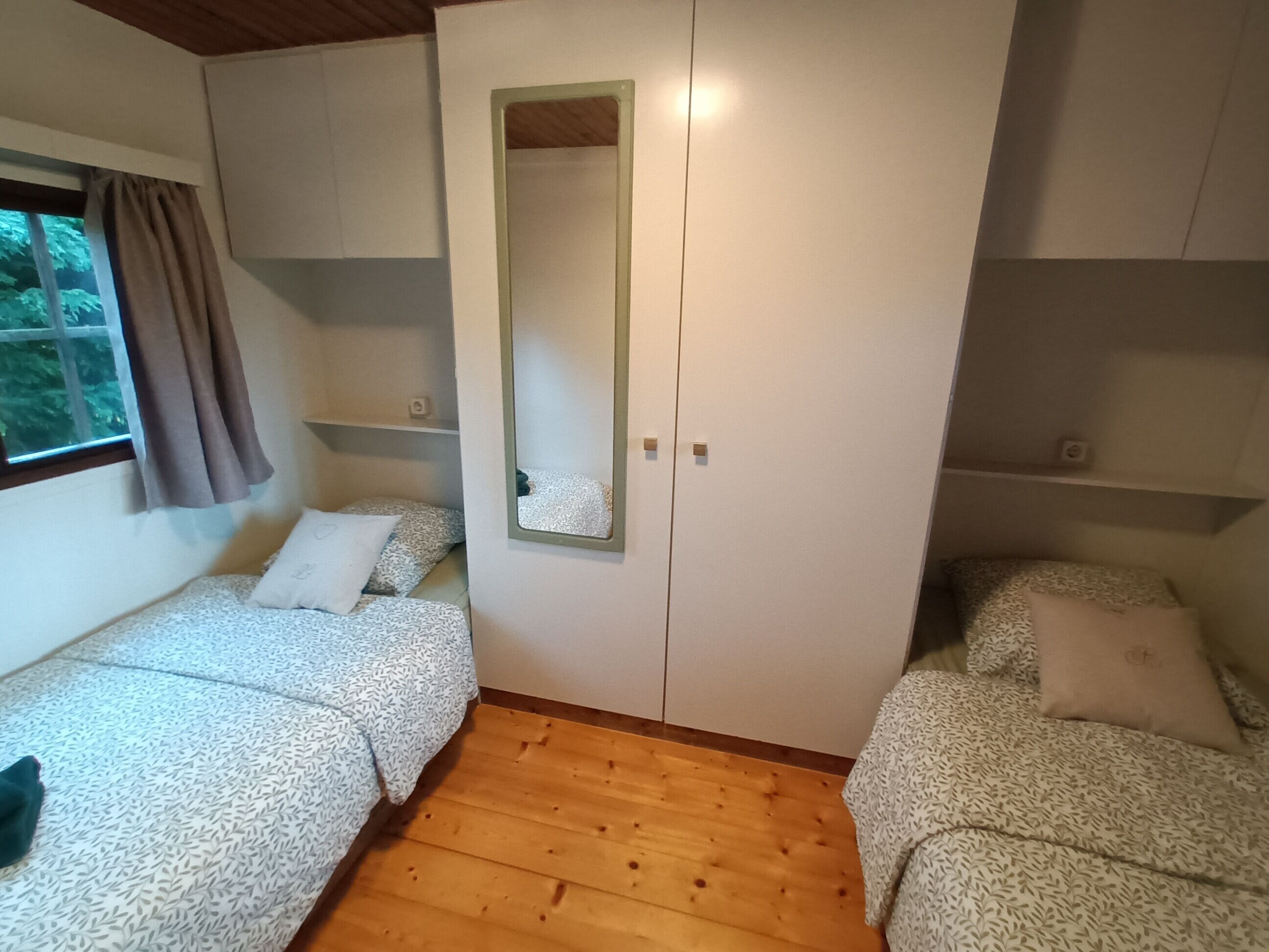 A room with two beds, a wardrobe, and a mirror.