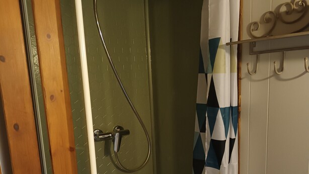 Een kleine, afgesloten douchehoek met een douchegordijn, een metalen douchekop en een witte wastafel.