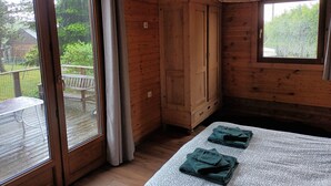 A wooden cabin room with a sliding glass door, a wooden wardrobe, and a bed with a patterned bedspread. - Charmante Cabane en Pleine Nature (Rhodes)