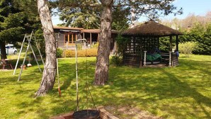 A gazebo with a thatched roof, surrounded by a well-maintained lawn and trees. - Charmante Cabane en Pleine Nature (Rhodes)