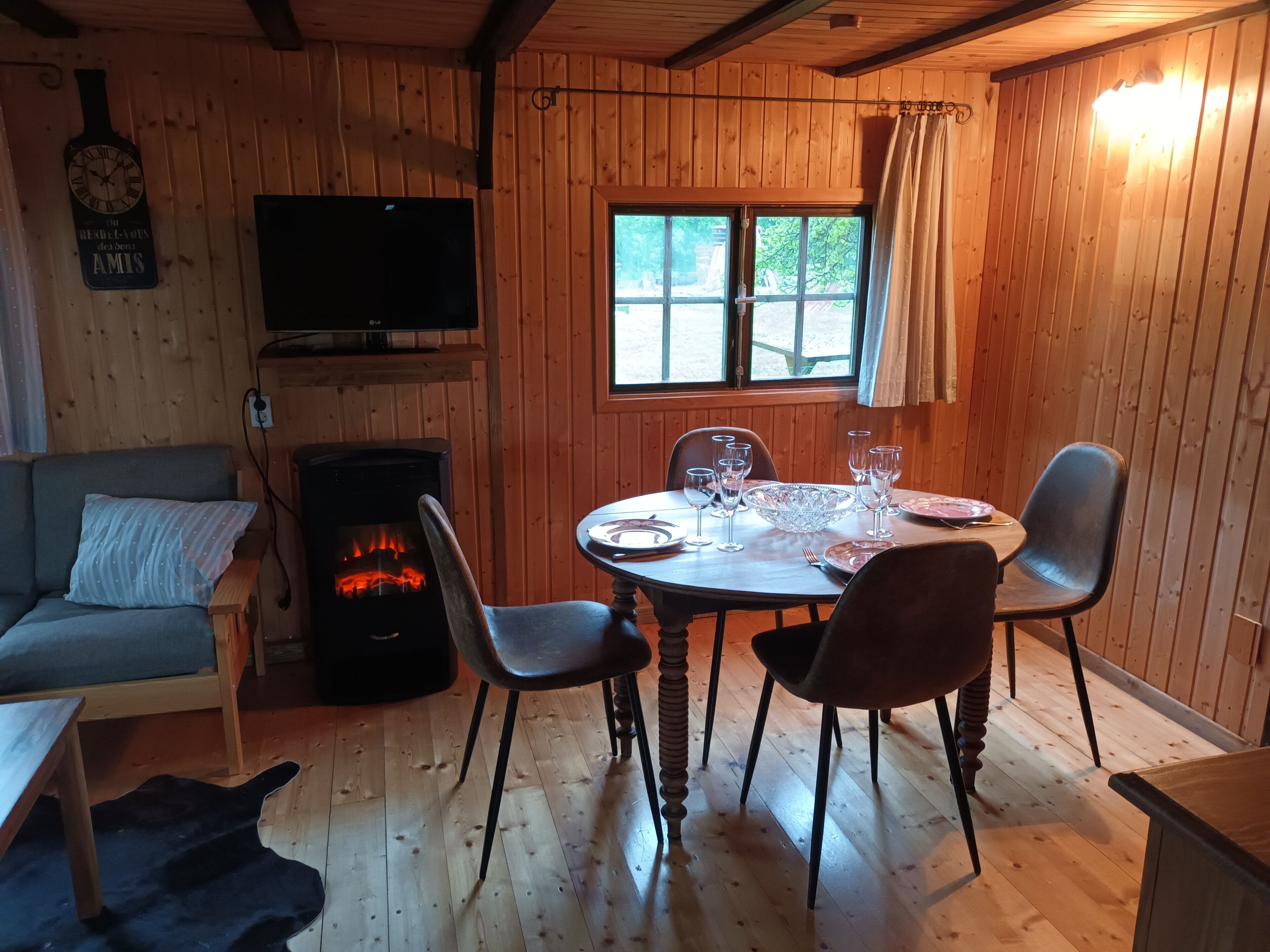 A cozy cabin interior with a wooden interior, a fireplace, a dining table set with plates and glasses, and a television mounted on the wall.