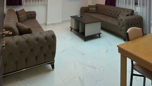A modern living room with a large ceiling screen displaying a sky scene, a sofa set, a coffee table, and a TV mounted on the wall. - Uluhan Residence (Trabzon)