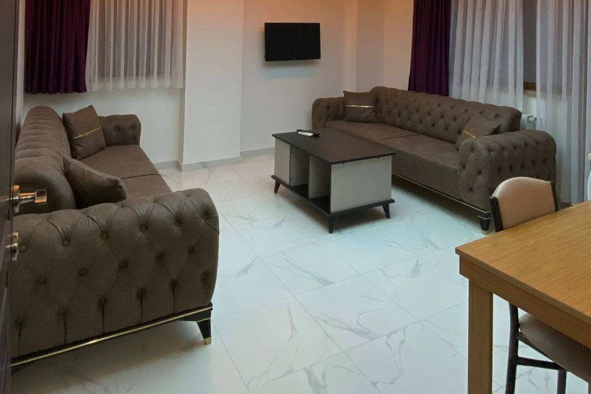 Un salon moderne doté d’un grand écran au plafond qui diffuse une scène de ciel, d’un ensemble de canapés, d’une table basse et d’un téléviseur fixé au mur.