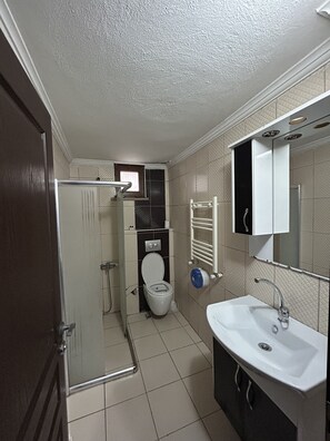 A bathroom with a toilet, shower, sink, and a mirror. - Uluhan Residence (Trabzon)